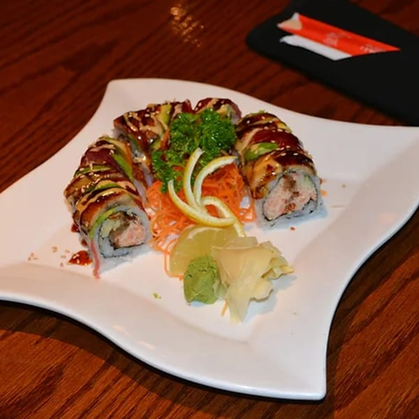 Wild Wok's sushi roll with avocado, sauce, sesame seeds, and garnishes on a white plate.
