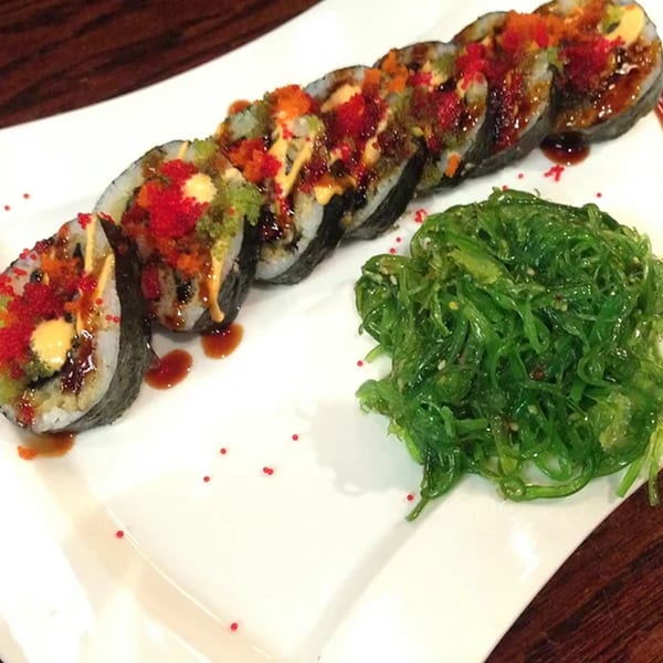 Wild Wok's sushi roll with colorful roe and sauce, served with a side of bright green seaweed salad.
