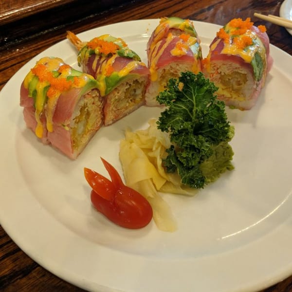 Four Wild Wok sushi rolls with avocado, tuna, sauce, and roe, garnished with ginger, wasabi, kale, and tomato.